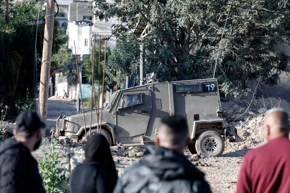 An Israeli military vehicle is parked outside the martyrs cemetery in Jenin refugee camp while Palestinians try to visit the tombs of relatives, Mar. 30, 2025.