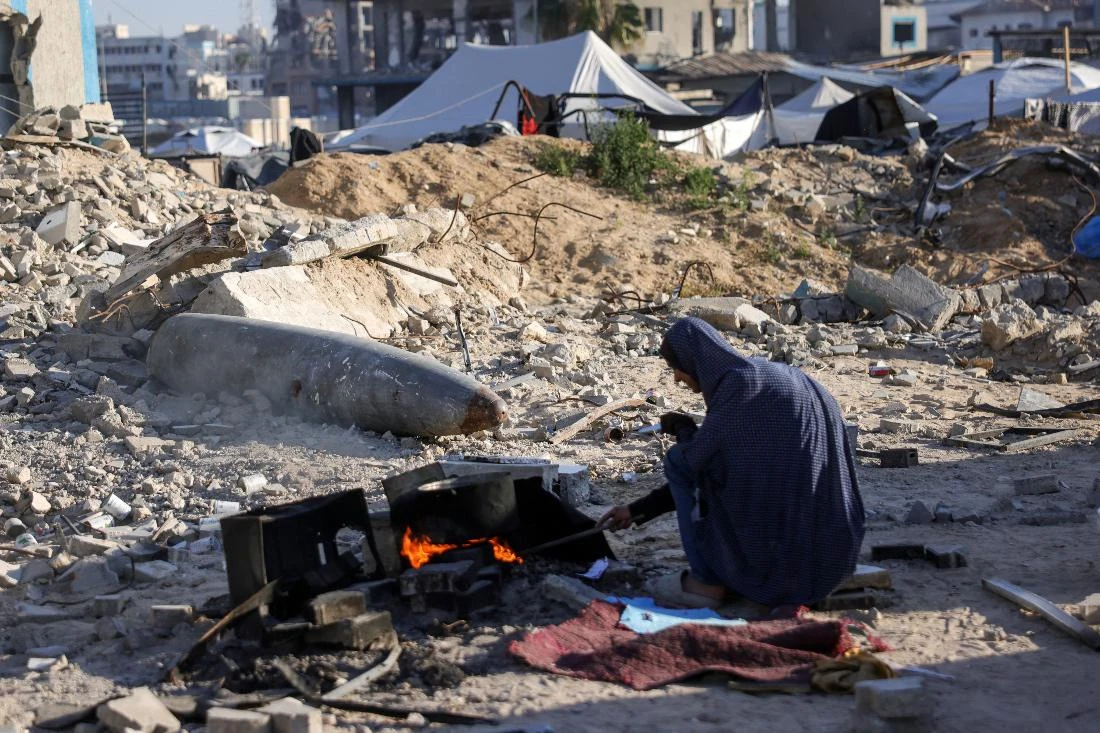 A displaced Palestinian woman cooks near an unexploded ordnance, with explosive materials removed and left behind by Israeli troops (AFP)