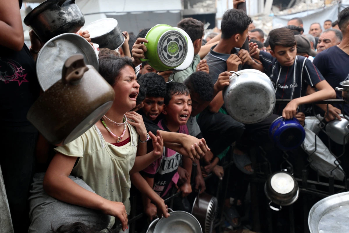 Children react as Palestinians wait to receive food cooked by a charity kitchen in Beit Lahia, northern Gaza Strip, on April 24, 2025. (REUTERS)