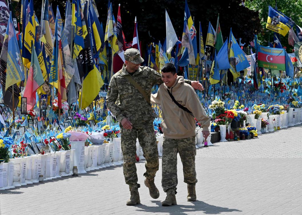Ukrainian servicemen react as they meet by chance at a makeshift memorial for the fallen Ukrainian and foreign fighters, on Independence Square in Kyiv on May 3, 2025. (AFP)
