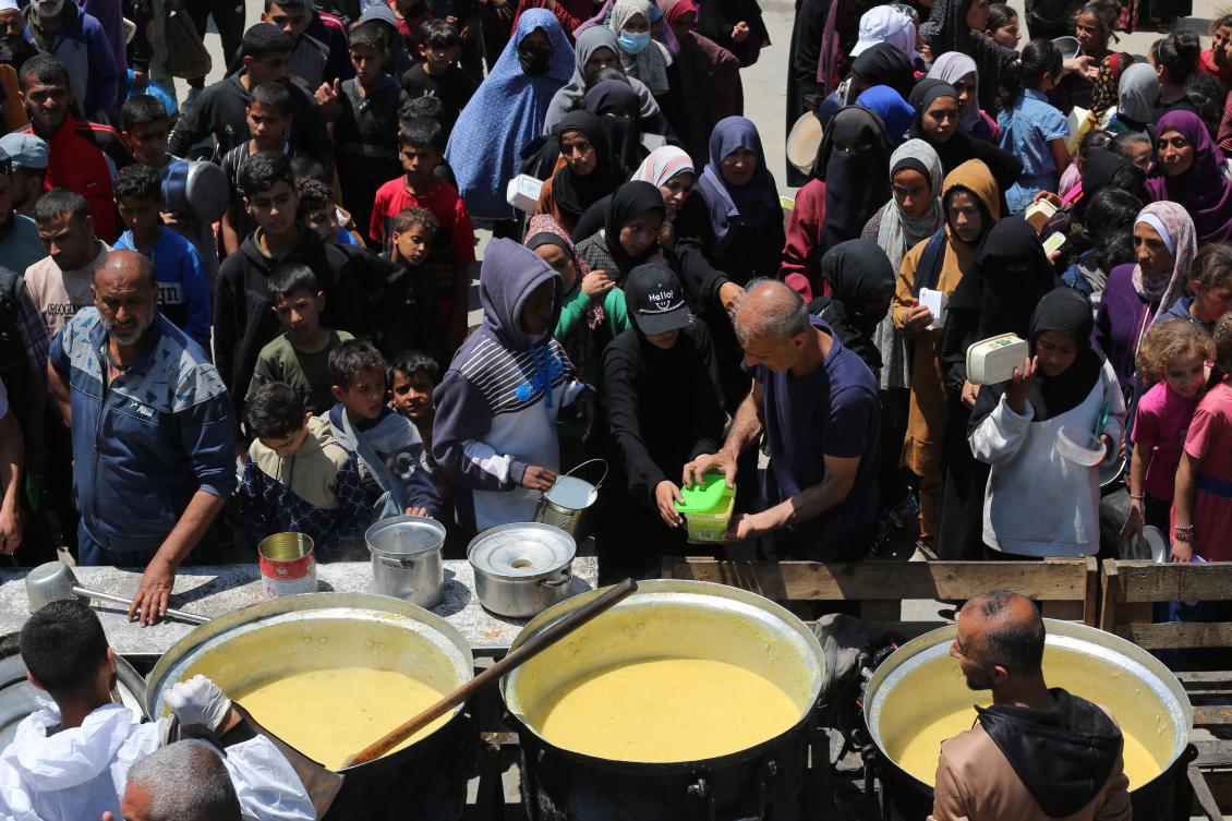 Palestinians queue for a portion of hot food distributed by a charity kitchen at the Nuseirat refugee camp in the central Gaza Strip on May 5, 2025. (AFP)