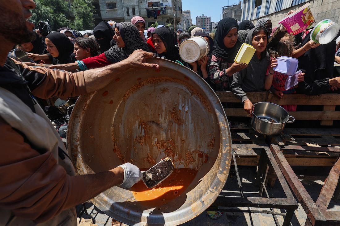 Palestinians queue for a portion of hot food distributed by a charity kitchen at the Nuseirat refugee camp in the central Gaza Strip. (File/AFP)