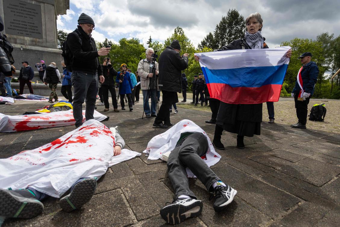 A woman with the Russian national flag reacts as Ukrainian activists lie on the pavement, simulating the bodies of victims, to protest the full-scale Russian invasion of Ukraine, at the mausoleum of Soviet soldiers in Warsaw, on May 9, 2025. (AFP)