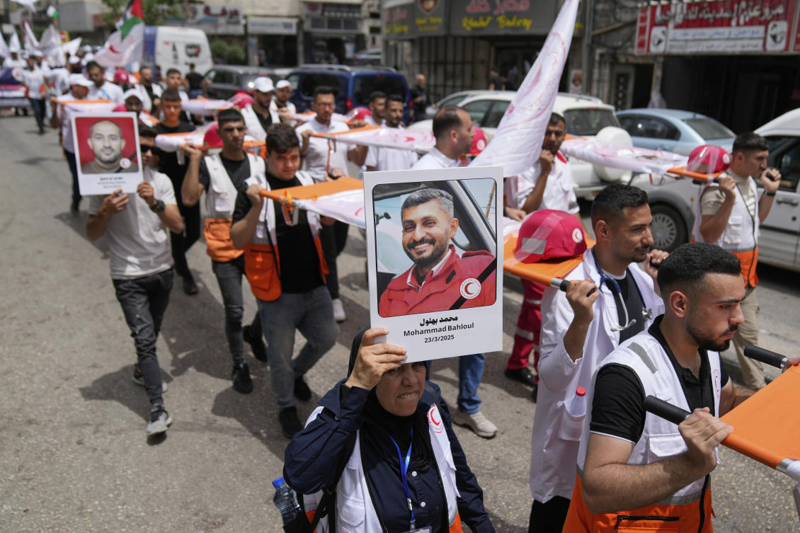 A paramedic holds posters with names and pictures of fellow relief workers who lost their lives in the line of humanitarian duty, during a symbolic funeral for 48 fallen Palestinian Red Crescent Society members during the Israel Hamas war in Gaza. (AP)