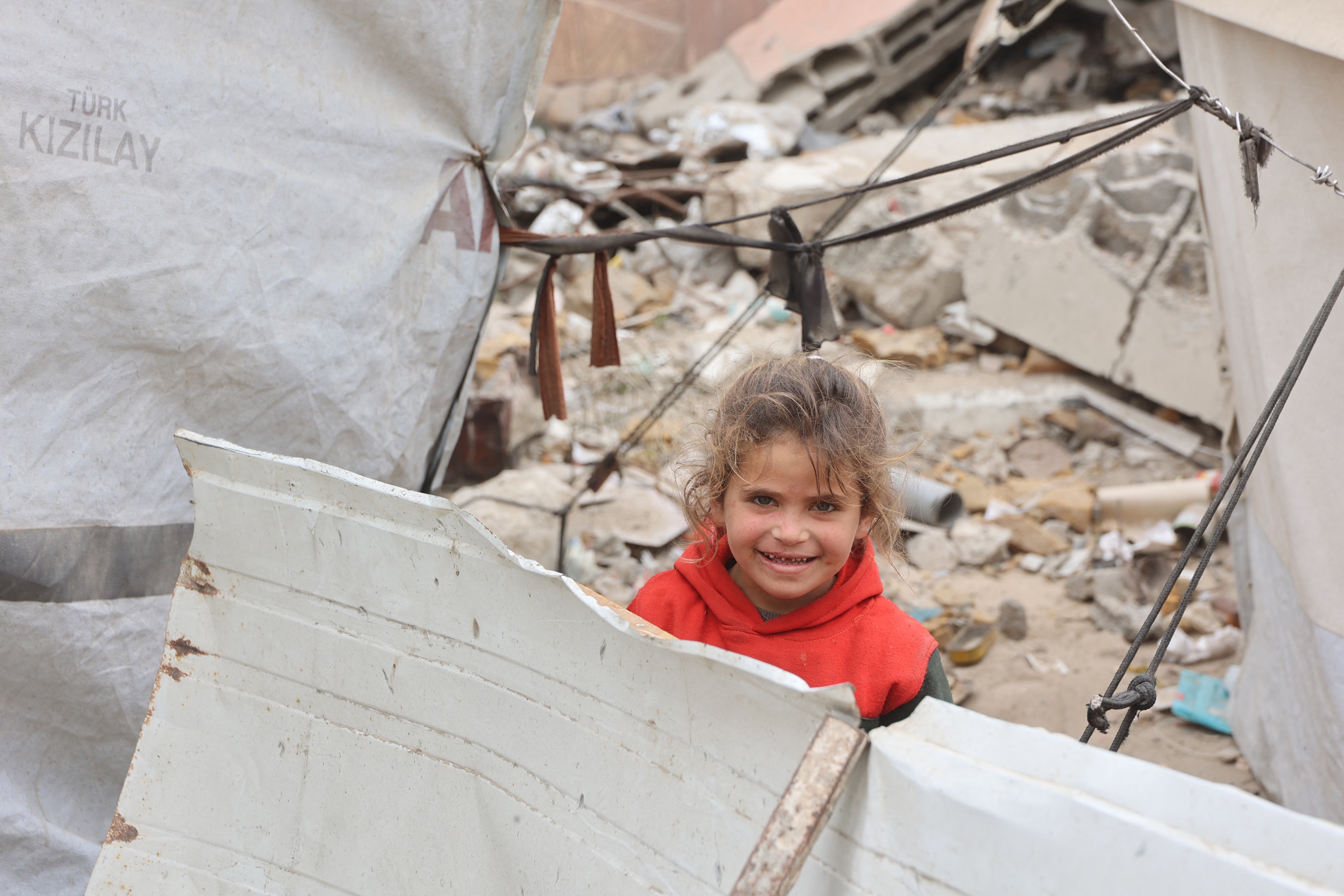A Palestinian girl smiles while playing near her tent at a makeshift displacement camp set up amid building rubble in Gaza City, May 12, 2025. (AFP)