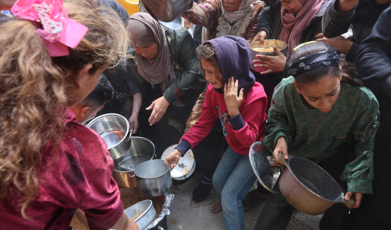 Palestinians shove to get a ration of hot food from a charity kitchen set up at the Islamic University campus in Gaza City on May 12, 2025. (AFP)