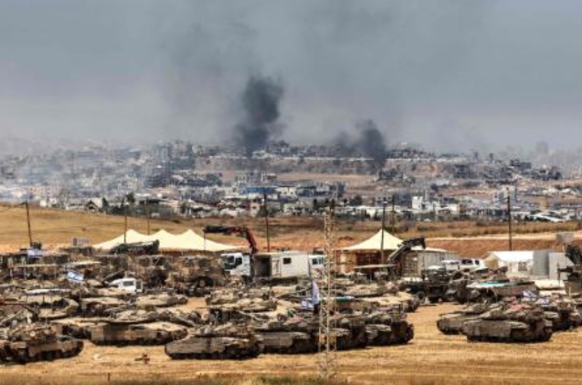 This picture taken from a position in southern Israel on the border with the Gaza Strip shows Israeli tanks and bulldozers deployed as smoke billows over destroyed buildings in Gaza during Israeli bombardment on May 17, 2025. (AFP)