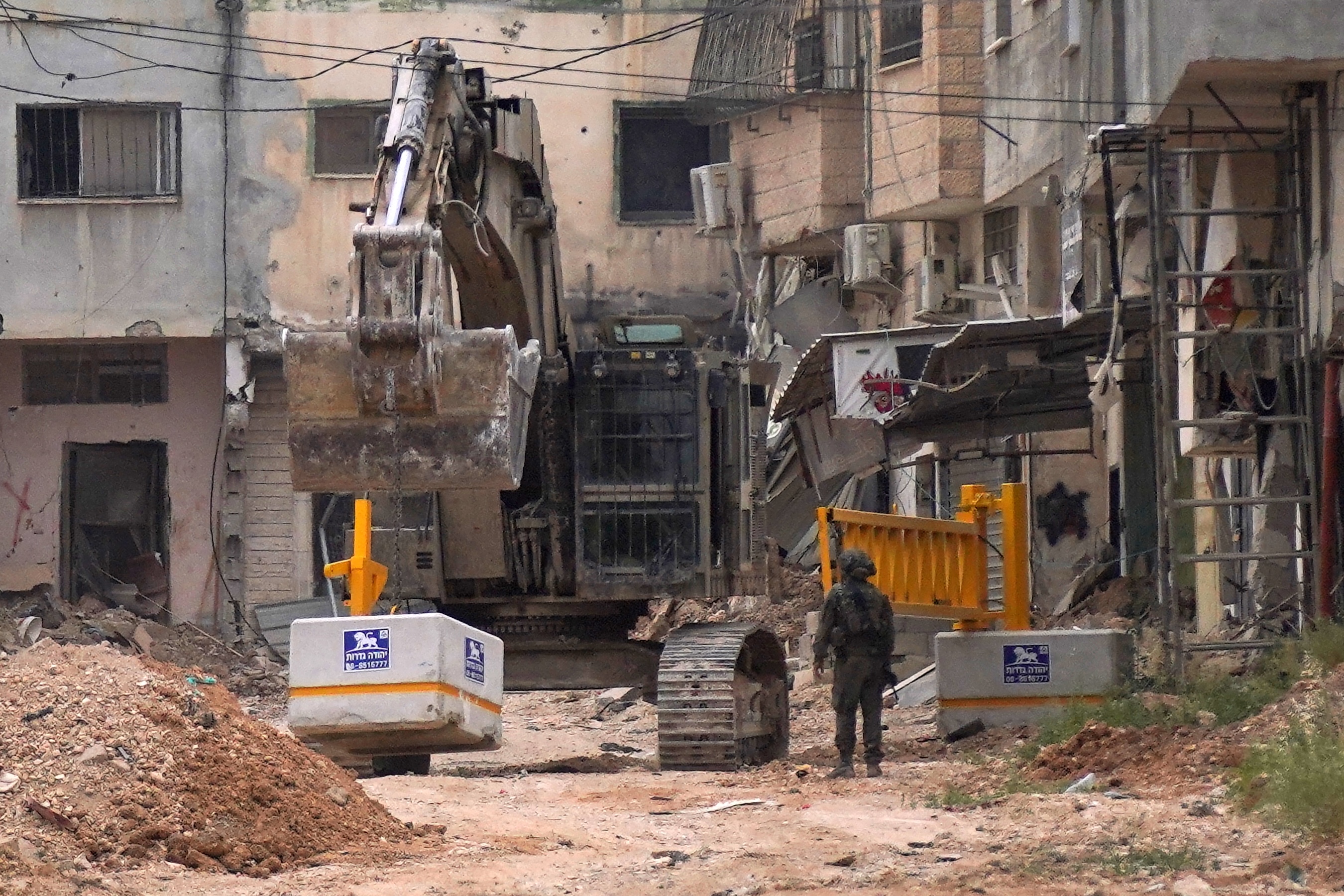 An Israeli soldier looks on as the army uses an excavator to install an iron gate at one of the entrances of the Jenin refugee camp in the occupied West Bank, Apr. 23, 2025. (AFP)