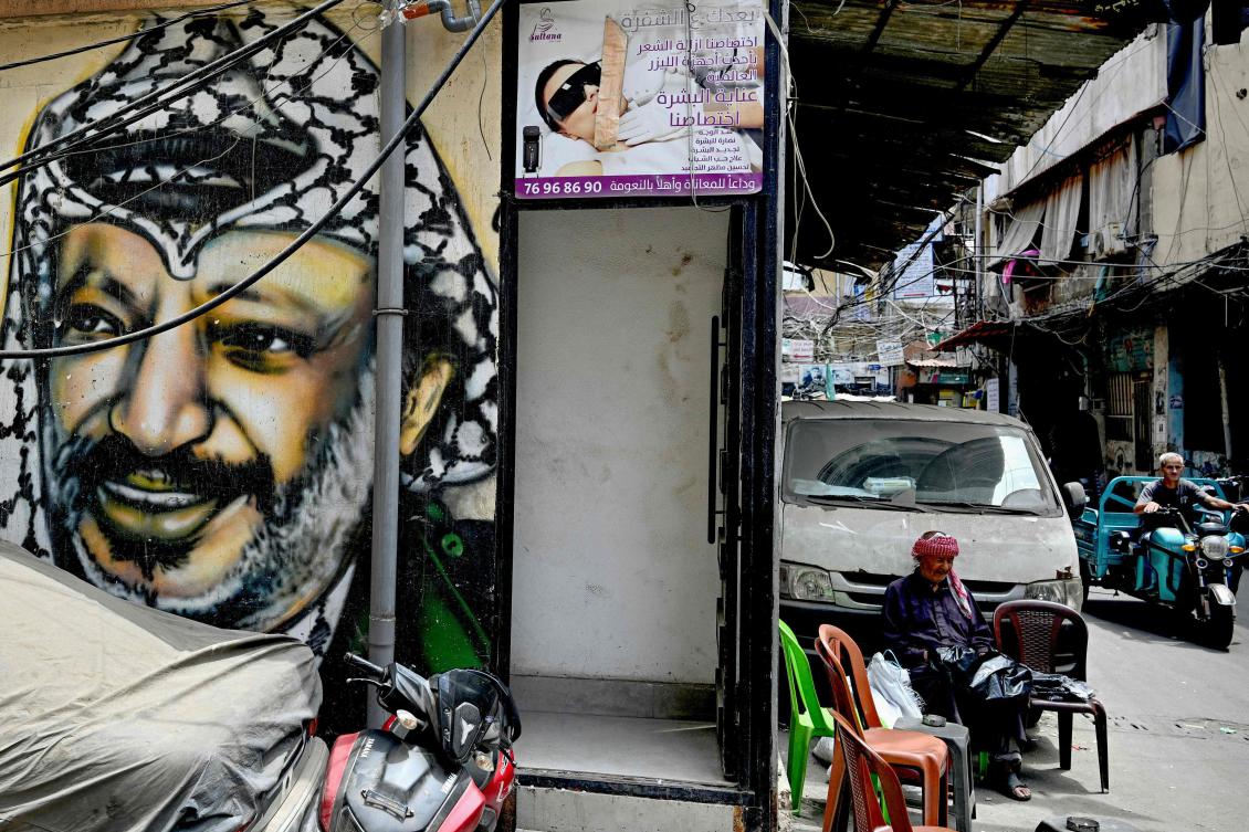 A man sits on a chair near a mural depicting late Palestinian president Yasser Arafat in an alley of the Burj al Barajneh camp for Palestinian refugees in Beirut, May 20, 2025. (AFP)