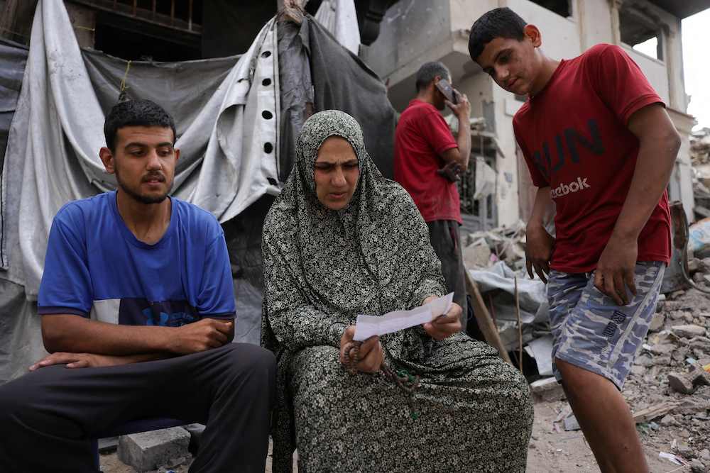 A Palestinian woman sits in front of a tent, as she holds a leaflet dropped by the Israeli army, warning people in Jabalia in the Northern Gaza Strip to flee toward the southern part of the territory, on May 22, 2025. (AFP)