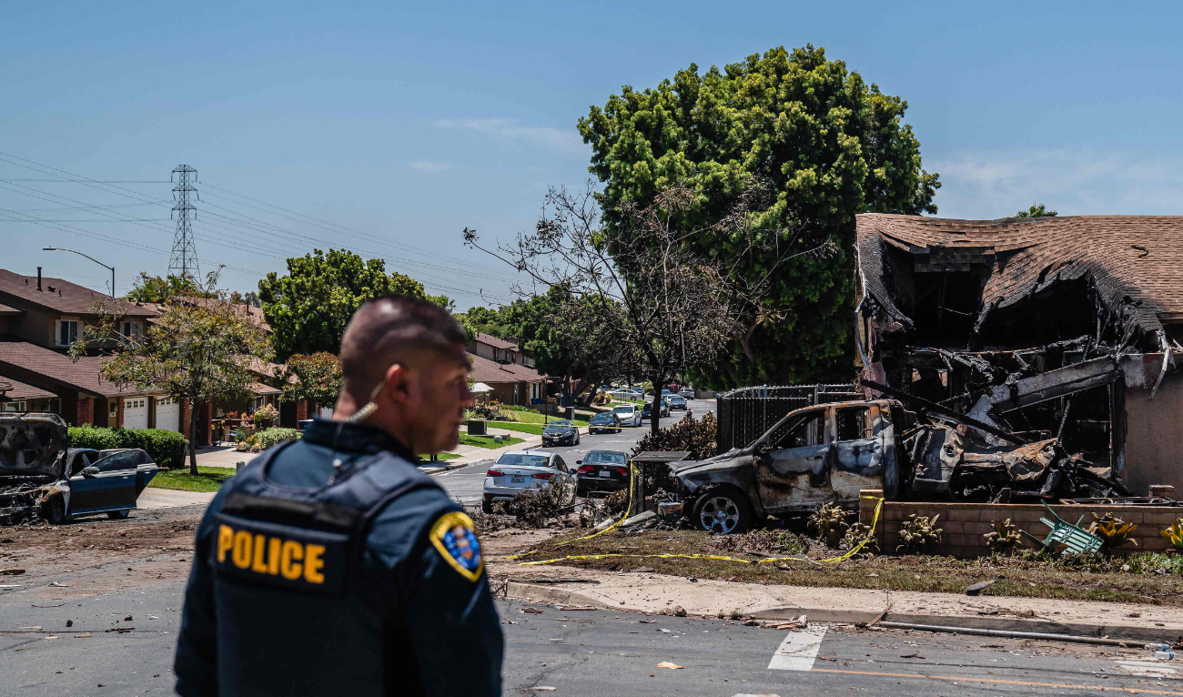A police officer stands in front of a house that was damaged after a small plane crashed into a neighborhood, setting homes and vehicles on fire on May 22, 2025 in San Diego, California. (AFP)