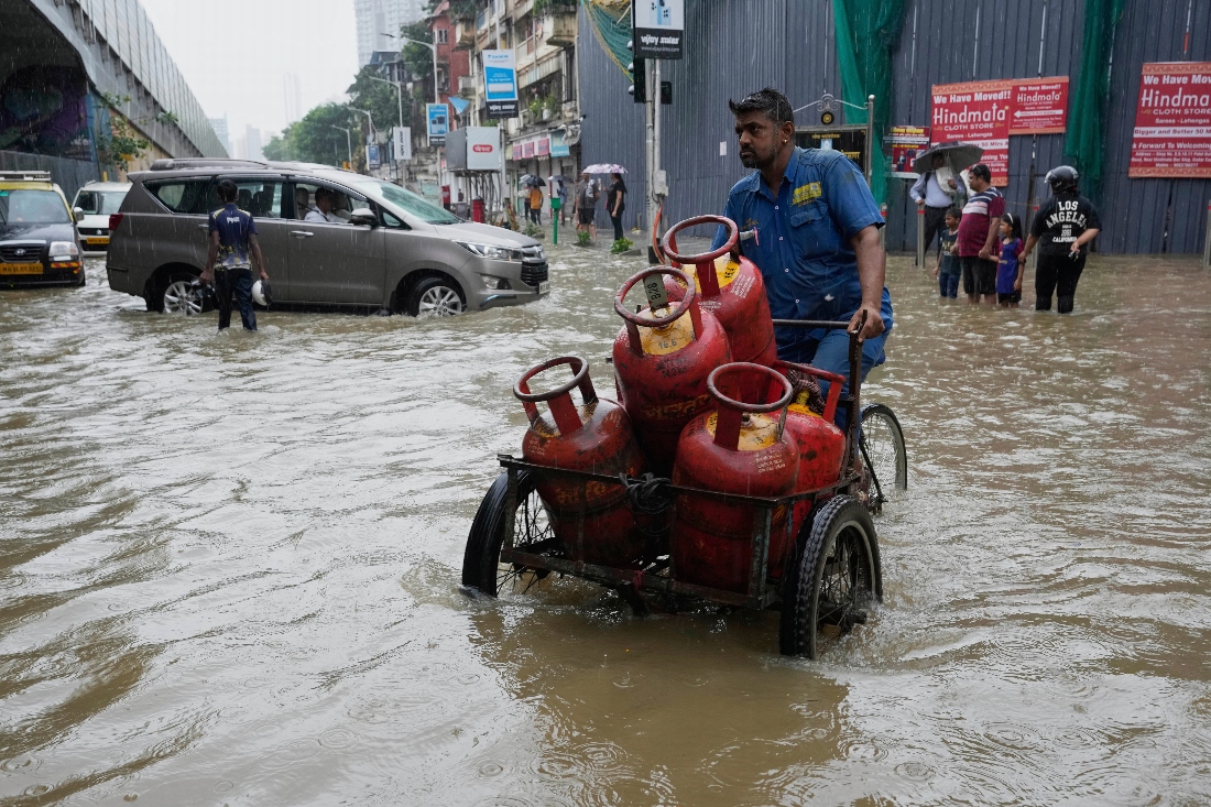 A worker transports cylinders through waterlogged streets during heavy rains in Mumbai, India. (AP)