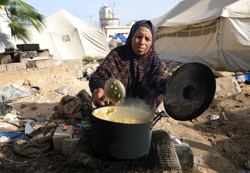 A Palestinian woman displaced by the Israeli military offensive, cooks food, in Gaza City May 11, 2025. (Reuters)