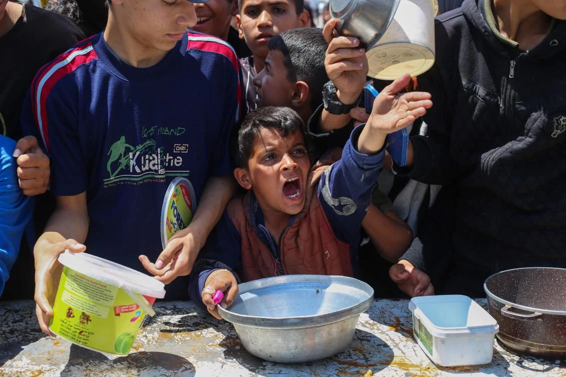 A Palestinian boy gestures as he waits for a portion of hot food distributed by a charity kitchen at the Nuseirat refugee camp in the central Gaza Strip, May 5, 2025. (AFP)