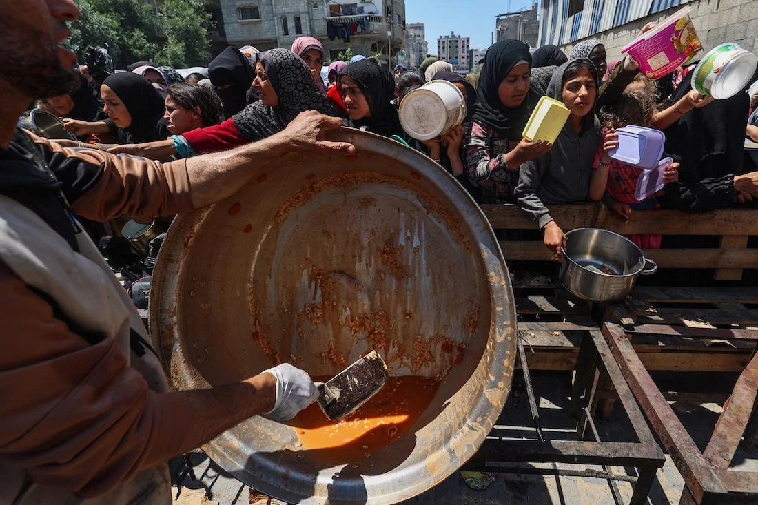 Palestinians queue for a portion of hot food distributed by a charity kitchen at the Nuseirat refugee camp in the central Gaza Strip. (File/AFP)