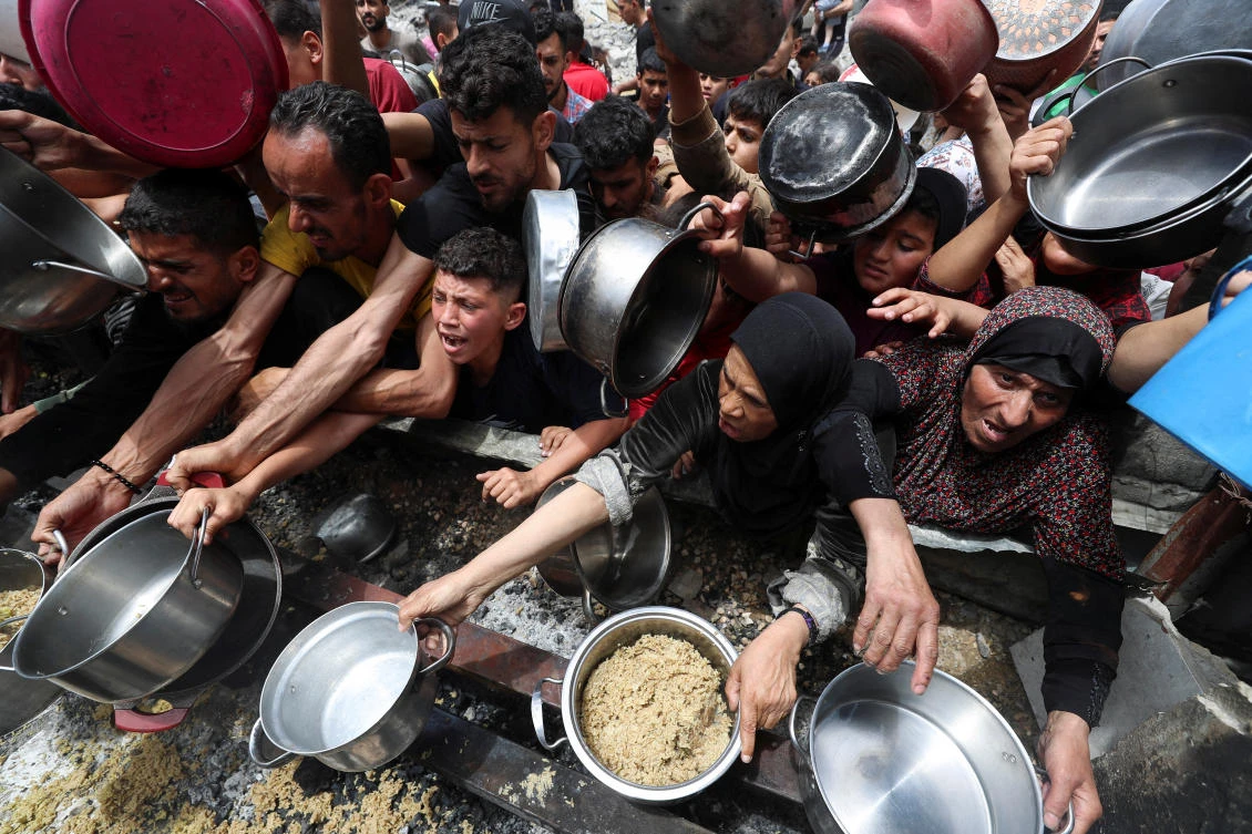 Palestinians wait to receive food cooked by a charity kitchen, in Jabalia, in the northern Gaza Strip, May 14, 2025. (Reuters)