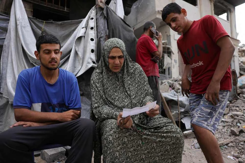 A Palestinian woman sits in front of a tent, as she holds a leaflet dropped by the Israeli army, warning people in Jabalia in the Northern Gaza Strip to flee toward the southern part of the territory, on May 22, 2025. (AFP)