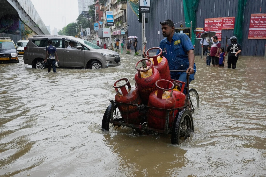 A worker transports cylinders through waterlogged streets during heavy rains in Mumbai, India. (AP)