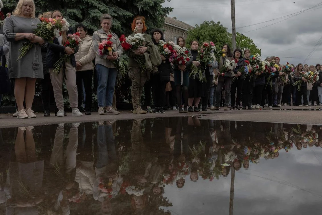 Attendees stand with flowers during the funeral ceremony of 17-year-old Roman Martyniuk, his 11-year-old sister Tamara Martyniuk and 8-year-old brother Stanislav Martyniuk, who were killed by a Russian missile strike, at a town hall in Korostyshiv, Zhytomyr region, on May 28, 2025. (AFP)