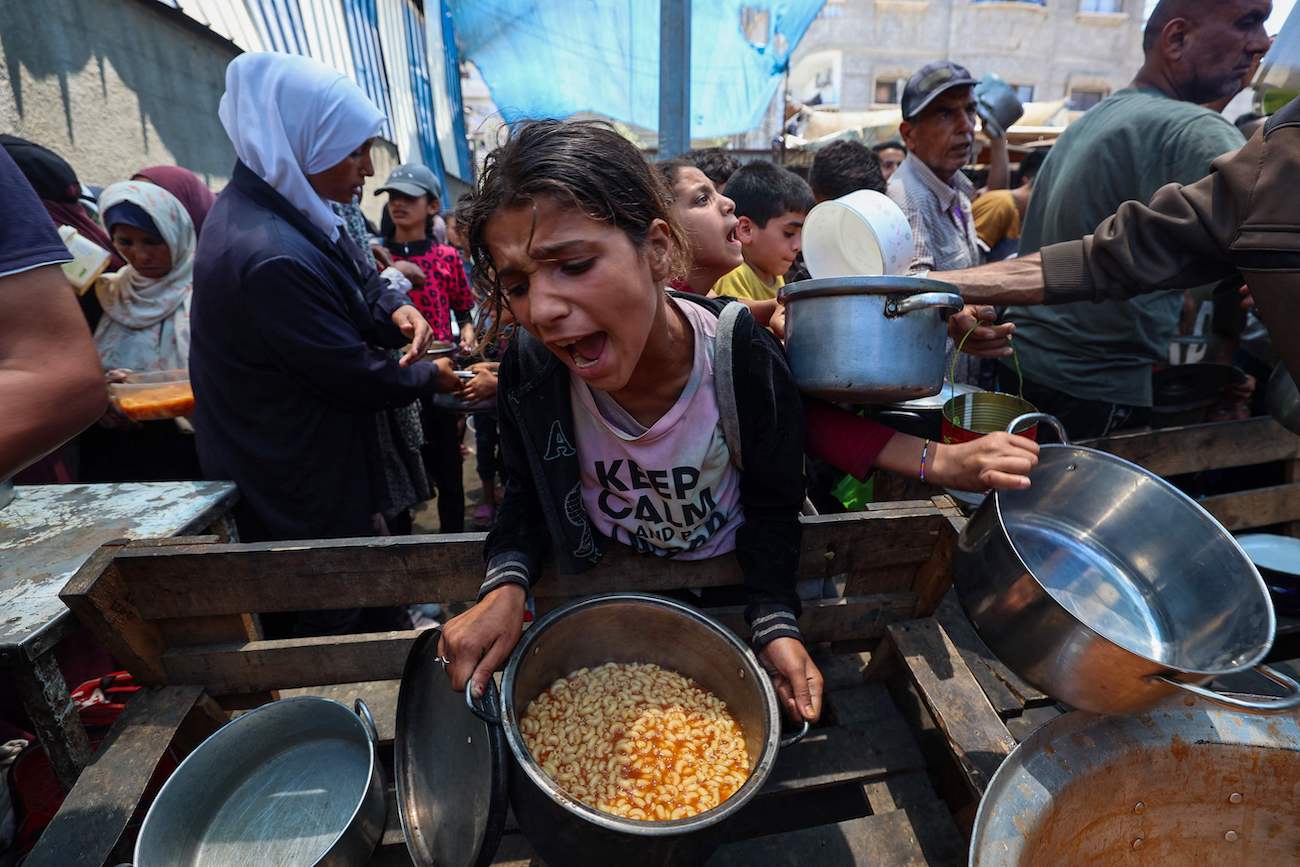 A girl reacts after receiving a cooked meal as others wait at a distribution point in Nuseirat, central Gaza Strip, June 2, 2025. (AFP)