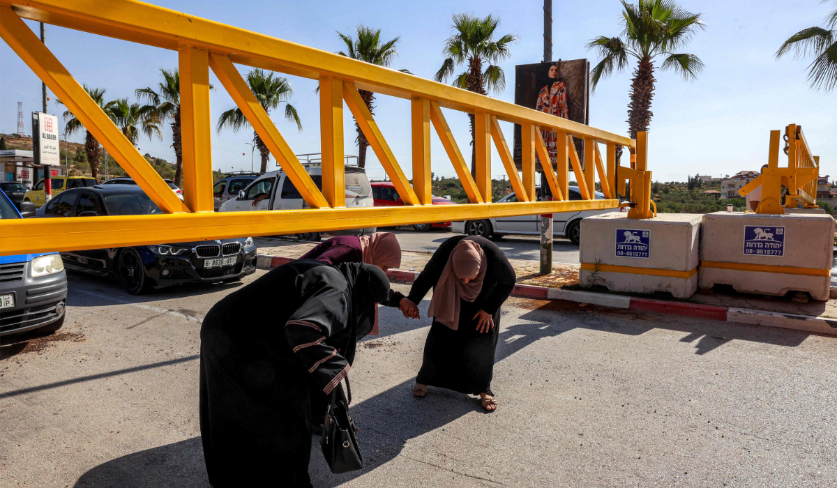 Palestinian women help each other as they bend to cross beneath a metal gate for vehicles set up by the Israeli army in the village of Turmus Ayya, north of Ramallah in the occupied West Bank, on June 1, 2025. (AFP)