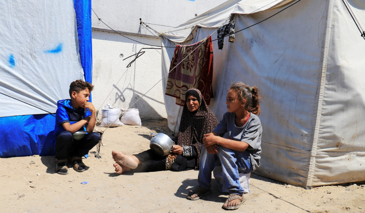A displaced Palestinian woman, Zeinab Abed, sits among children while holding an empty pot, as she waits to receive food from a charity kitchen, in Gaza City, June 3, 2025. (REUTERS)