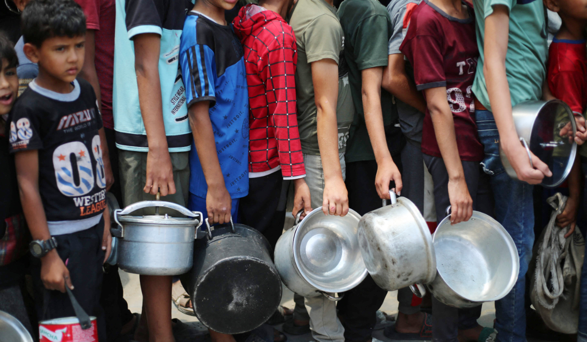 Palestinian boys carry pots as the queue at a hot meal distribution point in Nuseirat in the central Gaza Strip, June 4, 2025. (AFP)