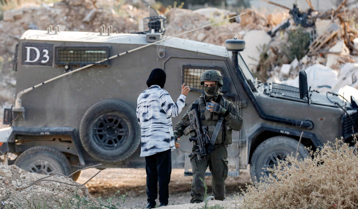 A woman speaks with an Israeli army soldier standing outside an armoured vehicle at a cemetery in Jenin in the occupied West Bank early on June 6, 2025 on the first day of Eid al-Adha, the Muslim feast of sacrifice. (AFP)