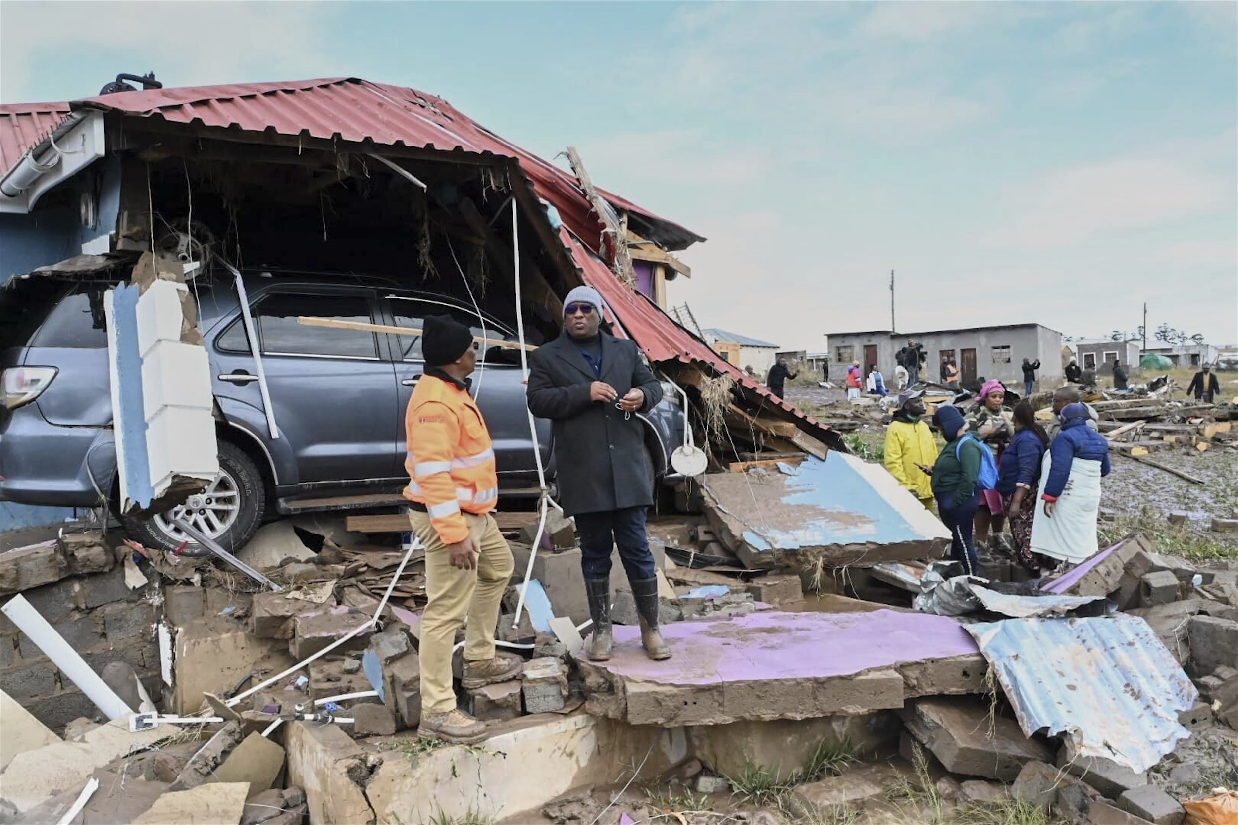 Eastern Cape premier Oscar Mabuyane, center stands with a local government official stand in front of a damaged home after flooding in the area, in Mthatha, South Africa, Wednesday, June 11, 2025. (AP Photo) (AP)