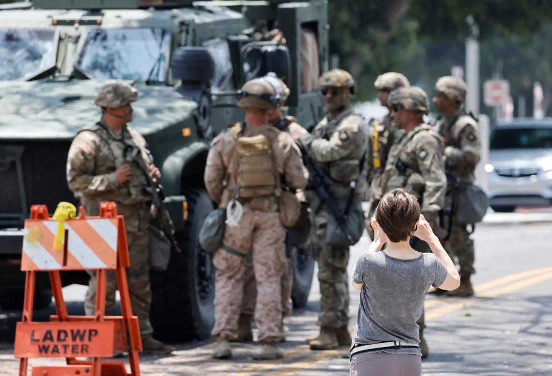 A pedestrian takes a photo as US Marines and California National Guard soldiers guard an entrance to the Wilshire Federal Building on June 13, 2025 in Los Angeles, California. (Getty Images via AFP)