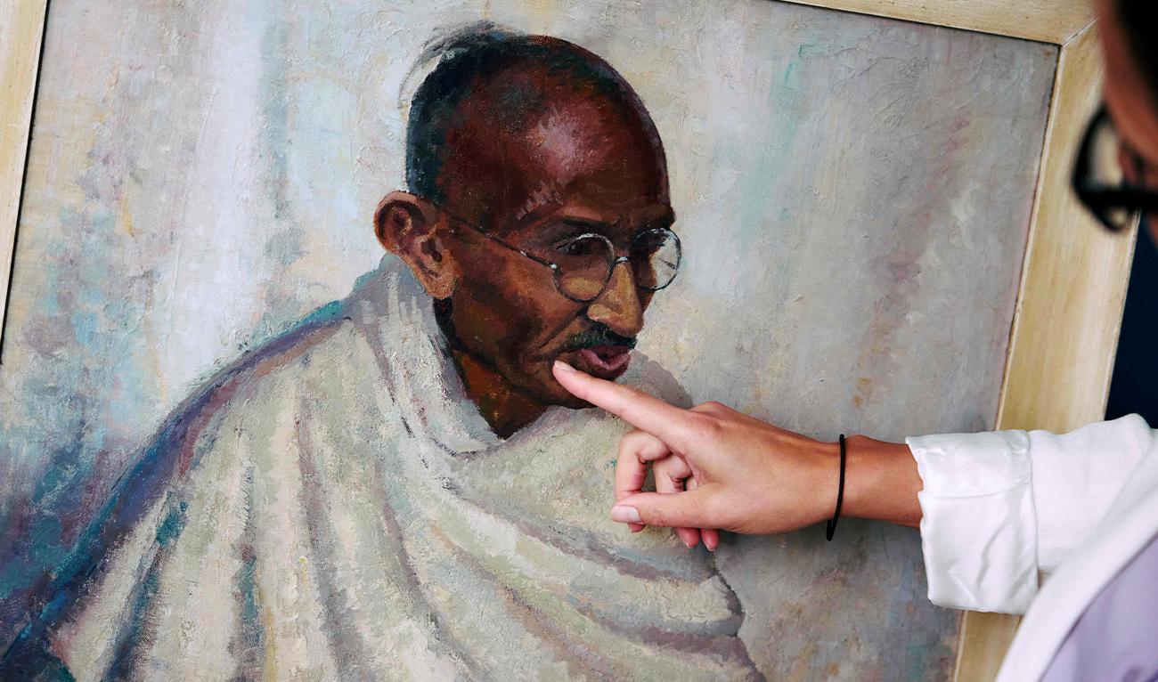 Rhyanon Demery, Bonhams Head of Sale for Travel and Exploration, points out the spot where the now-restored painting by British-American artist Clare Leighton of Indian independence leader Mahatma Gandhi was once damaged at Bonhams auction house in London on June 9, 2025. (AFP)