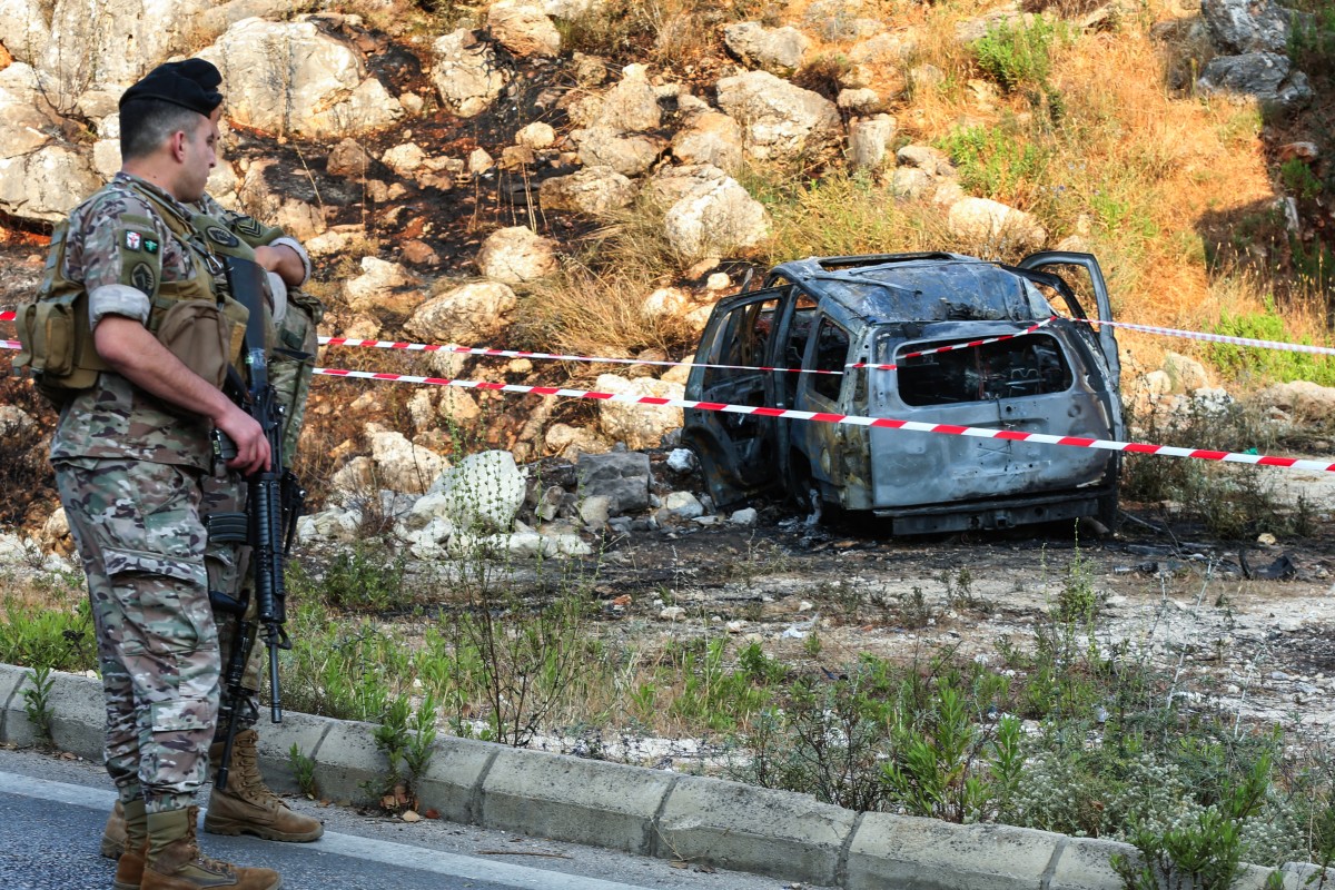 Army officers stand guard near a cordoned-off carcass of a car that was targeted in a reported Israeli drone attack in the southern Lebanese town of Al-Numairiyah, June 9, 2025. (AFP)