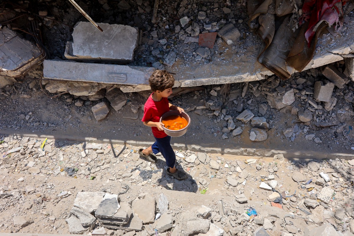 A Palestinian boy carries a bowl of food collected at a charity kitchen providing hot meals in Rimal neighbourhood in Gaza City, June 18, 2025. (AFP)