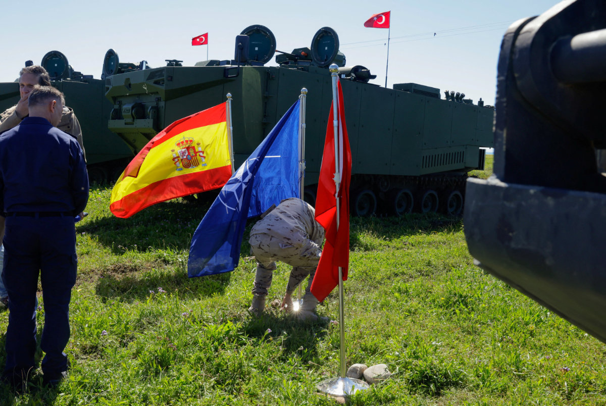 A Spanish soldier places a NATO flag next to a Spanish flag and Turkish flag during the NATO Exercise Dynamic Mariner 25 military drill training in Barbate, Spain, on March 28, 2025. (REUTERS)