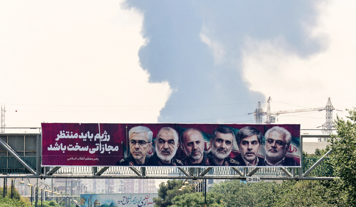 Portraits of Iranian military generals and nuclear scientists, killed in Israel's June 13 attack are displayed above a road, as a plume of heavy smoke rises from an oil refinery in southern Tehran, after it was hit in an overnight Israeli strike, on June 15, 2025. (AFP)