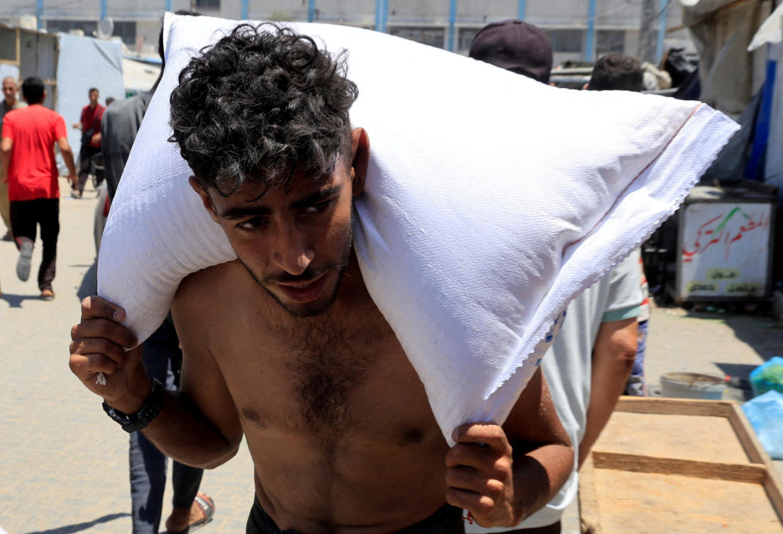 A Palestinian carries a sack of flour as people gather to receive aid supplies in Khan Younis, in the southern Gaza Strip, June 26, 2025. (REUTERS)