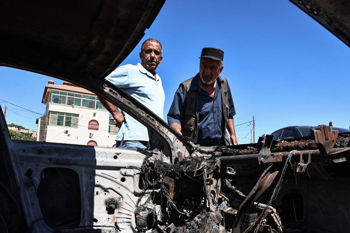 Palestinian men check a burnt car after an Israeli settler attack the previous day in Kafr Malik in the Israeli-occupied West Bank, June 26, 2025. (AFP)