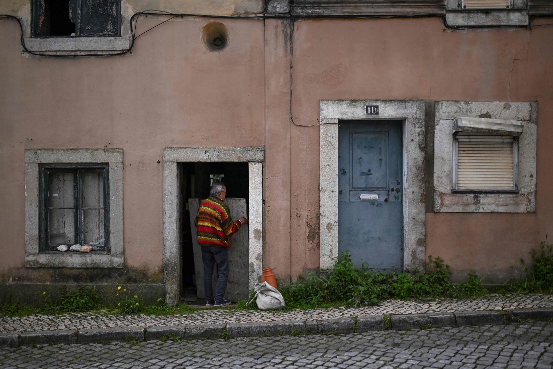 An 80 year old retired kitchen assistant, uses a board to block the entrance of the abandoned house where he lives, in Belem, Lisbon. (AFP)