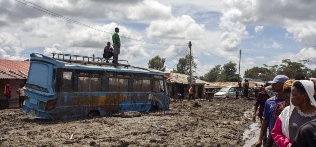 Two men stand on top of a bus as others gather to assess damages at a street covered on mud following landslides and flooding triggered by heavy rainfall in Katesh, Tanzania in 2023. (AFP)