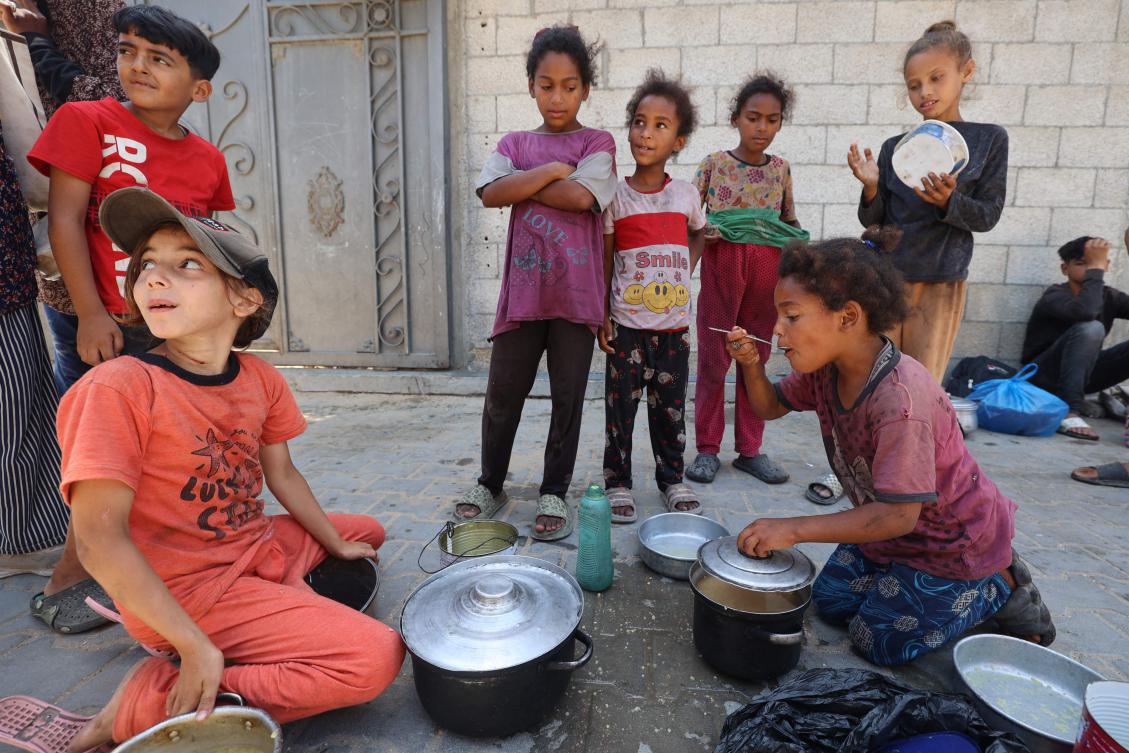 Palestinian children eat from pots after collecting a hot meal at a food distribution point in Nuseirat, in the central Gaza Strip, on June 30, 2025. (AFP)