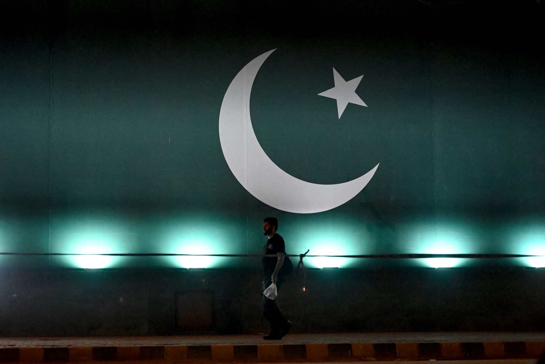 A man walks past Pakistan's national flag on the eve of the country’s independence day, in Karachi, August 13, 2024. (AFP)