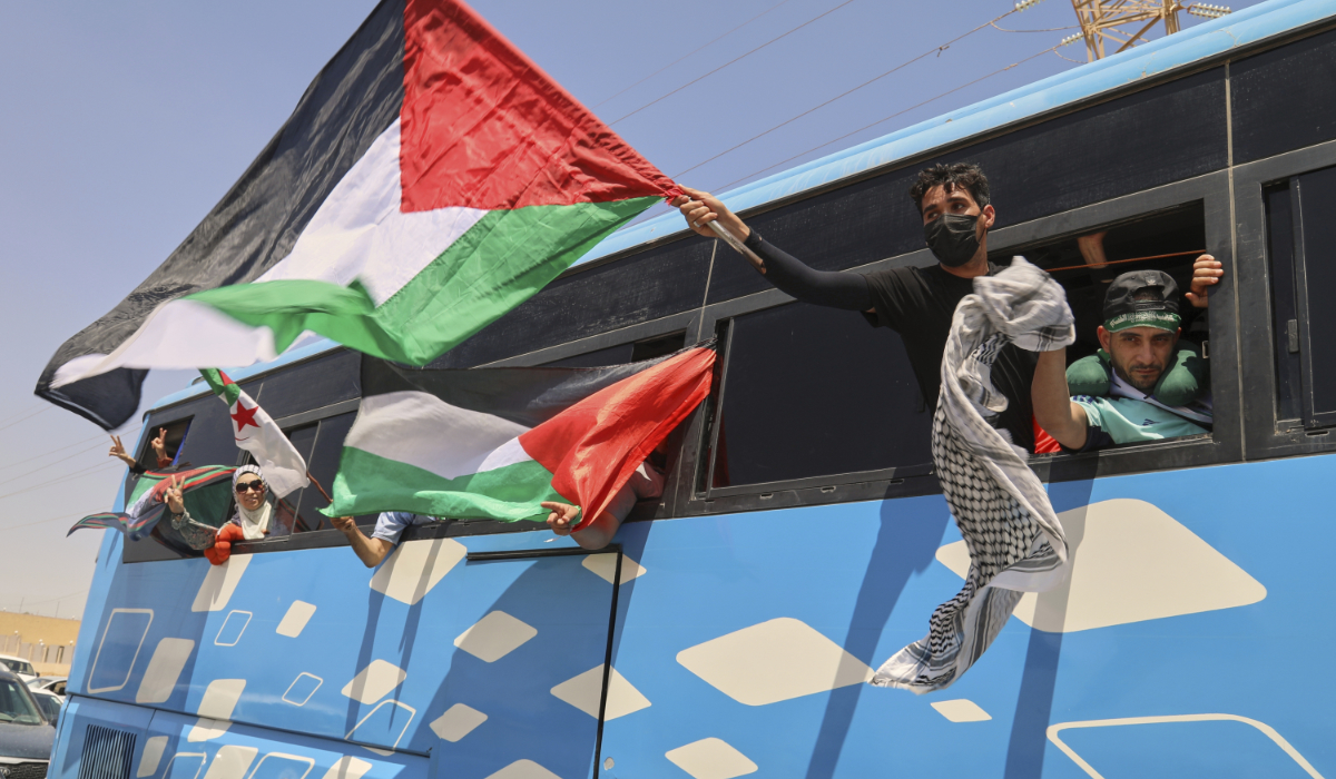 Members of a humanitarian convoy wave Palestinian flags from a bus as the group travels toward Gaza via Egypt, in Zawiya.