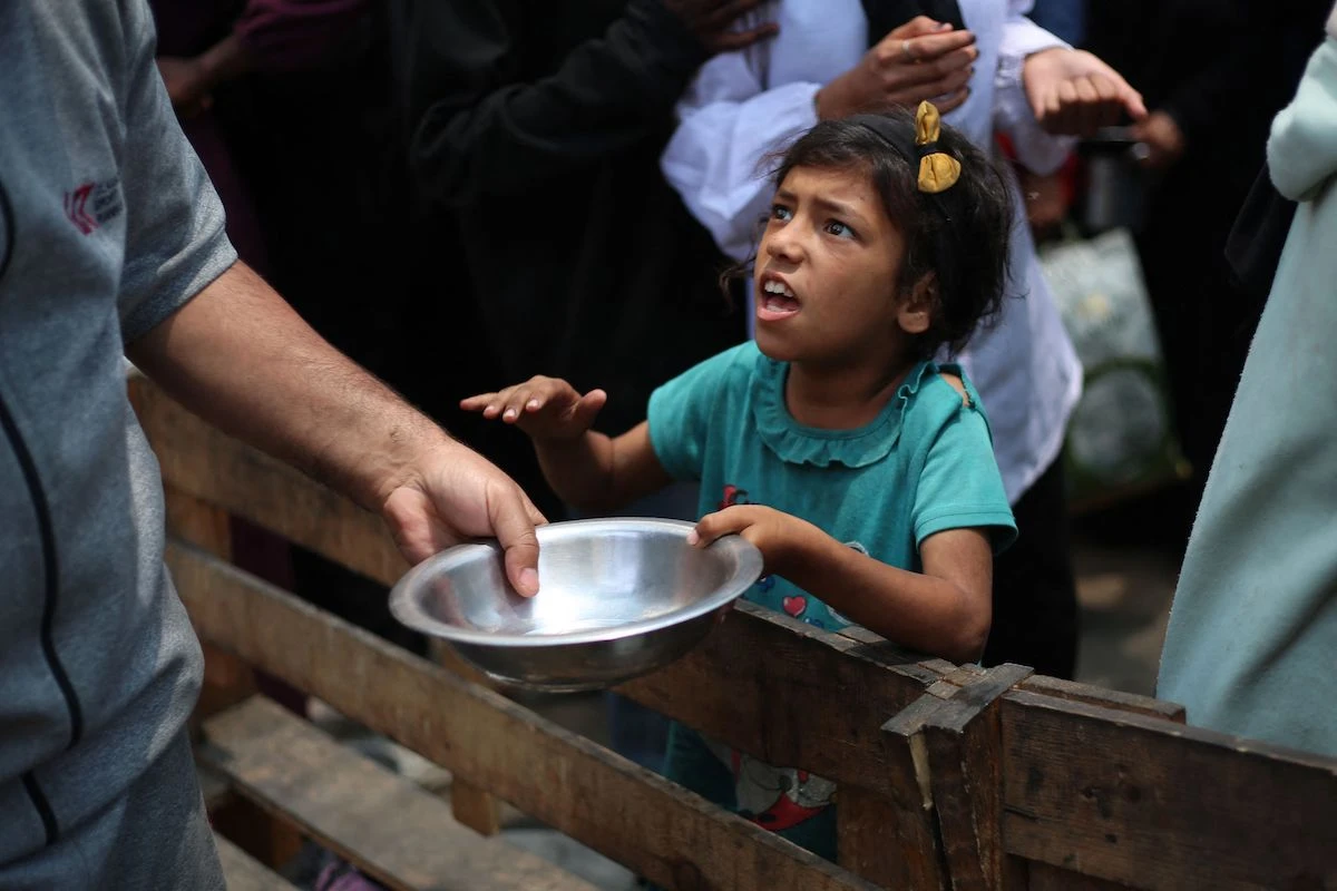 A Palestinian girl holds an empty pan at a hot meal distribution point in Nuseirat in the central Gaza Strip Wednesday. (AFP)