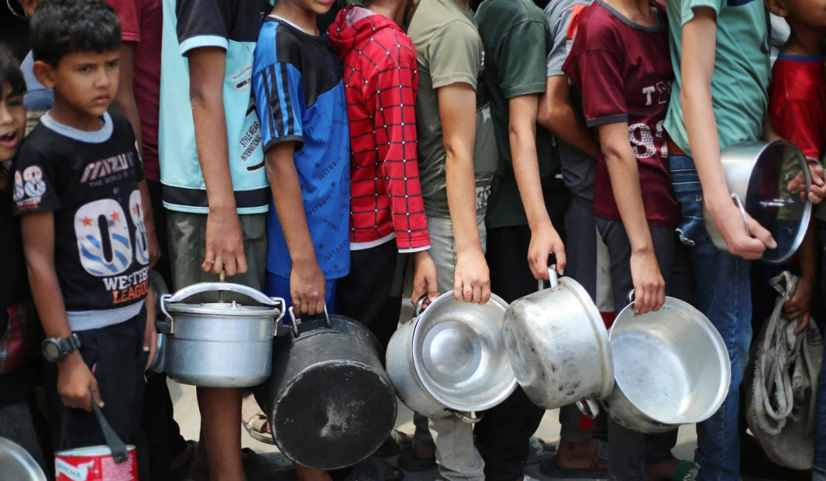 Palestinian boys carry pots as the queue at a hot meal distribution point in Nuseirat in the central Gaza Strip, June 4, 2025. (AFP)