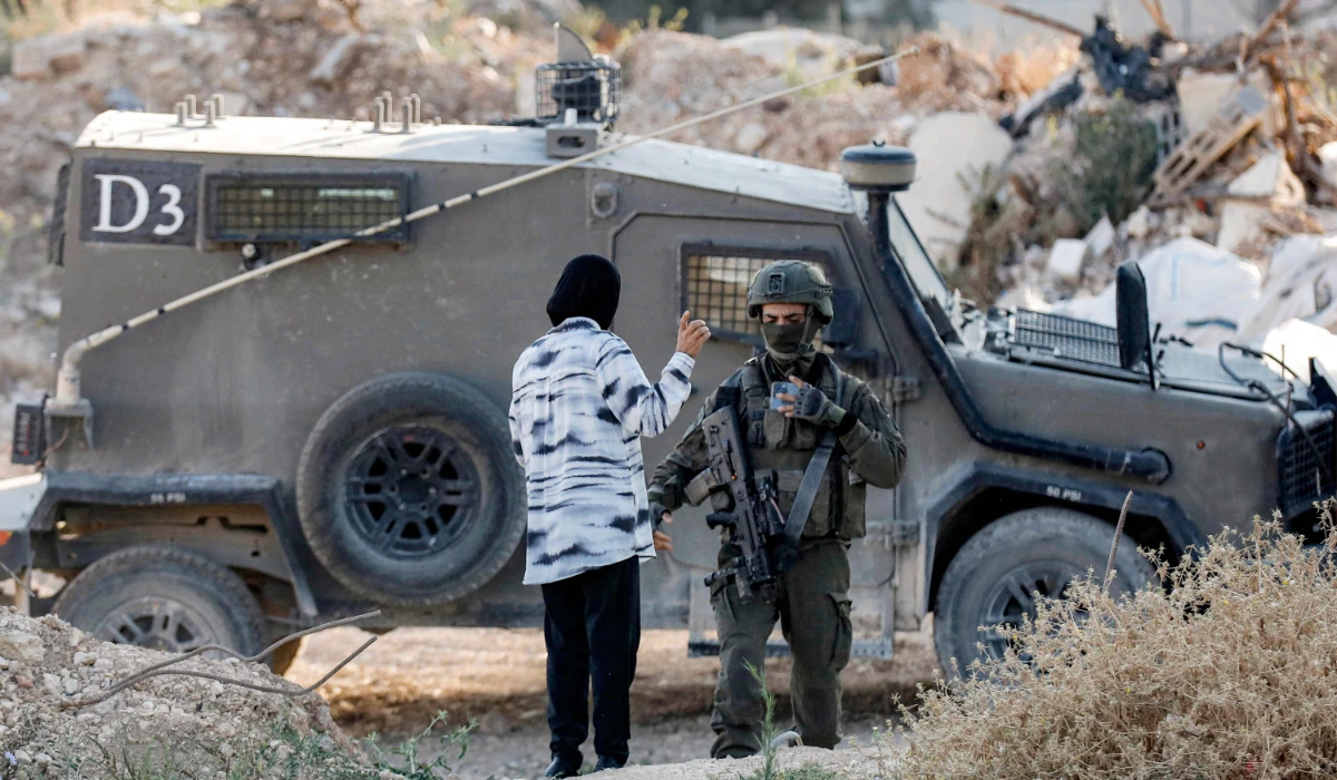 A woman speaks with an Israeli army soldier standing outside an armoured vehicle at a cemetery in Jenin in the occupied West Bank early on June 6, 2025 on the first day of Eid al-Adha, the Muslim feast of sacrifice. (AFP)