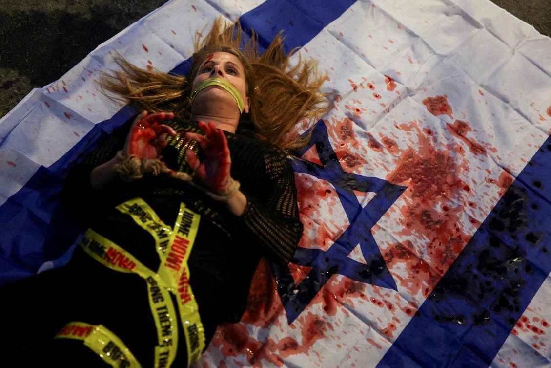 A demonstrator in Tel Aviv lies on an Israeli flag stained with fake blood at a protest demanding the release of all Israeli hostages kidnapped by Hamas. (Reuters)