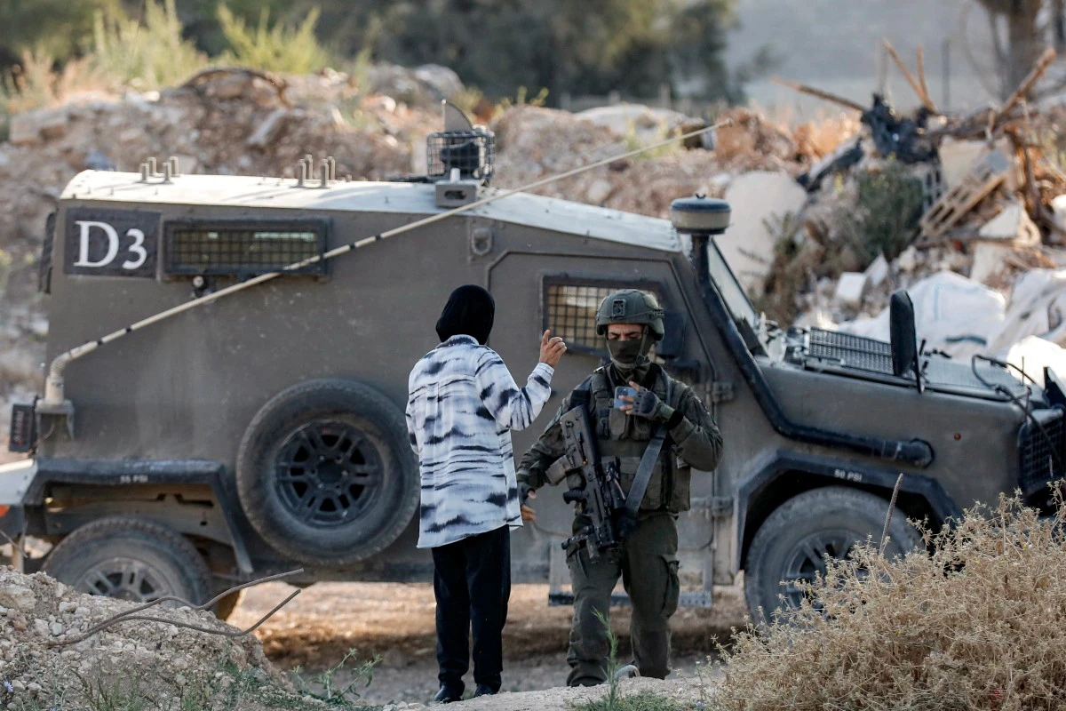 A woman speaks with an Israeli army soldier standing outside an armoured vehicle at a cemetery in Jenin in the occupied West Bank, June 6, 2025. (AFP)