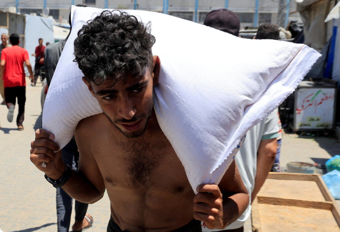 A Palestinian carries a sack of flour as people gather to receive aid supplies in Khan Younis, in the southern Gaza Strip, June 26, 2025. (REUTERS)