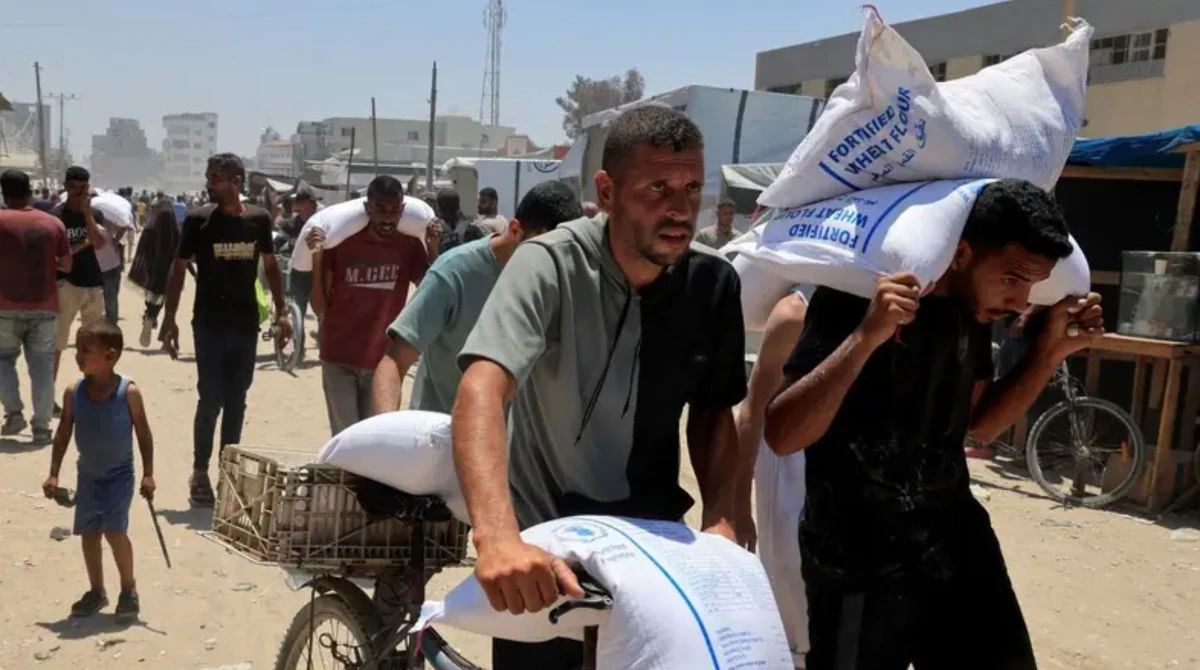Palestinians carry sacks of flour as they gather to receive aid supplies in Khan Younis, in the southern Gaza Strip, June 26, 2025. (Reuters)