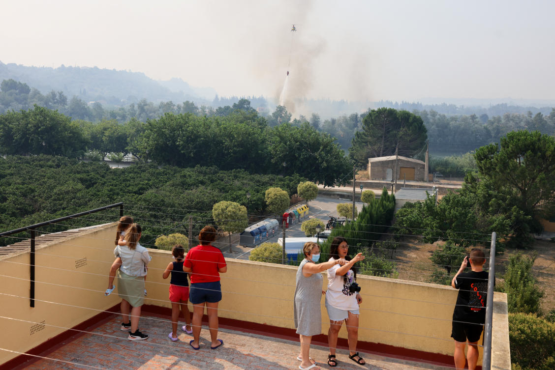 People watch as a helicopter flies to help extinguish an ongoing wildfire in Xerta, which is one of the confined villages in the Tarrragona province in Catalonia, Spain on July 8, 2025. (Reuters)